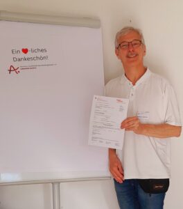 Der Vorsitzende der Alzheimer Gesellschaft Recklinghausen steht vor einem Schild mit der Aufschrift Ein Herzliches dankeschön und hält den Spendengutschein in der Hand
